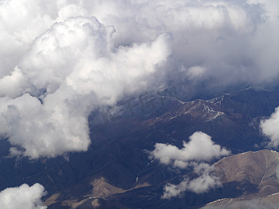 航拍美景白天白云下的山雪飞机上透过白云航拍山峦摄影图配图