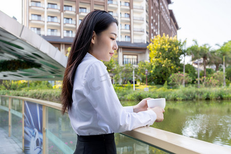 商务下午商务女性湖边拿着咖啡侧脸摄影图配图