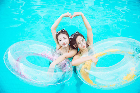 泳衣美女摄影照片_夏日清凉白天抱着游泳圈的两个美女泳池比心摄影图配图