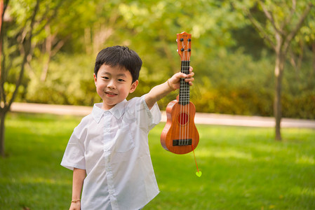 户外小孩摄影照片_夏季白天男孩户外弹吉他摄影图配图