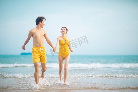 爱情情人节白天一对黄色情侣装情侣沙滩手拉手奔跑摄影图配图