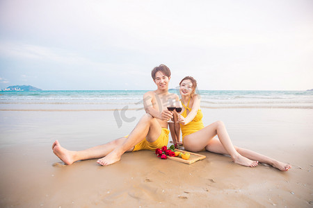 海边沙滩度蜜月摄影照片_爱情蜜月白天喝红酒的情侣沙滩捧杯摄影图配图