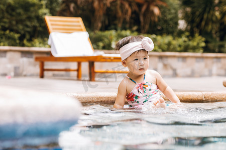 夏天儿童白天穿粉色泳装的女童户外泳池边玩水摄影图配图