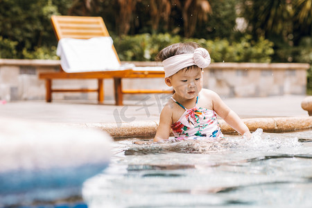 亲子设施摄影照片_夏天儿童白天穿粉色泳装的小女孩户外泳池玩水摄影图配图