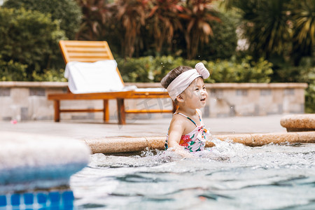 泳衣小孩摄影照片_夏天儿童白天穿泳衣的小女孩户外泳池玩水摄影图配图