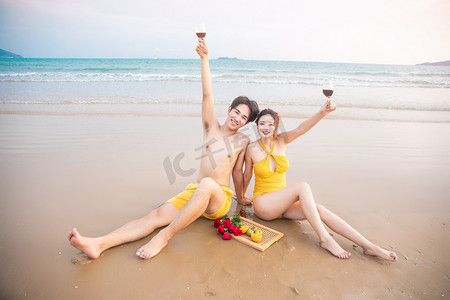 海边沙滩度蜜月摄影照片_爱情蜜月白天喝红酒的情侣沙滩高举酒杯摄影图配图