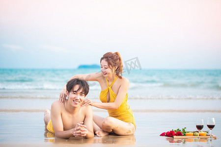 促销防晒摄影照片_爱情白天一对情侣户外沙滩按摩背部擦防晒摄影图配图