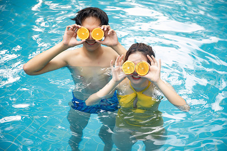 人物表白摄影照片_人物夏天情侣泳池用橙子挡眼摄影图配图