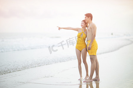 爱情七夕情侣摄影照片_爱情白天一对情侣沙滩指向远方摄影图配图