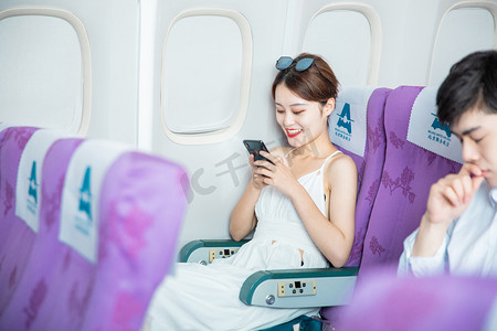 空姐漫画摄影照片_空乘白天飞机上的女乘客飞机客舱内看手机摄影图配图