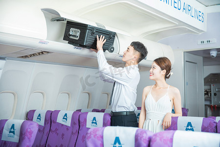 客舱服务白天男乘务员和女乘客飞机客舱内放好行李箱摄影图配图