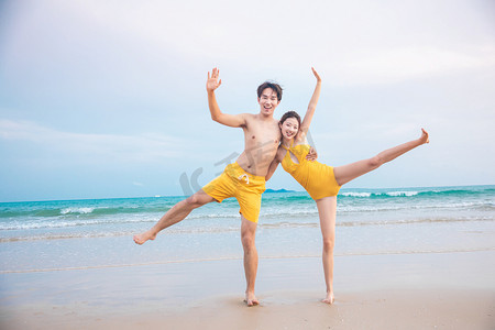 海边水花摄影照片_情人节白天一对情侣户外沙滩踢起水花摄影图配图