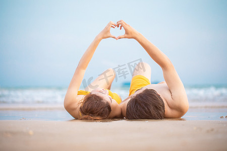 爱心白天一对情侣沙滩躺着比心摄影图配图