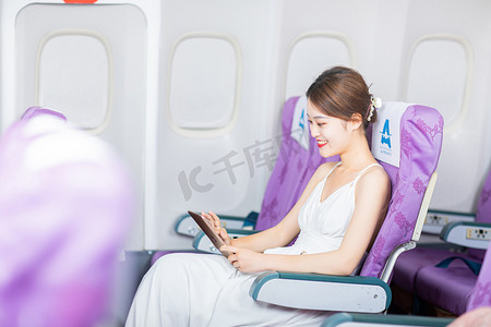 坐飞机摄影照片_坐飞机白天飞机上的女乘客飞机客舱内看书看手机摄影图配图
