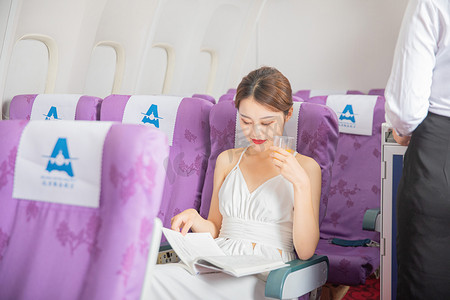 乘飞机旅行摄影照片_商务白天乘飞机的美女客舱内看书摄影图配图