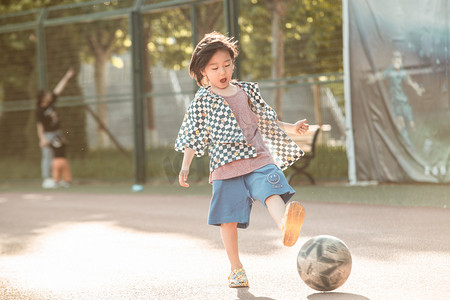小孩踢足球摄影照片_夏日儿童人像操场踢足球摄影图配图