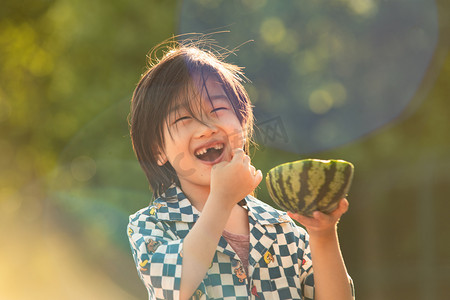 夏日重先摄影照片_夏日儿童人像白天长发小男孩阳光下抱着西瓜开心大笑摄影图配图人物