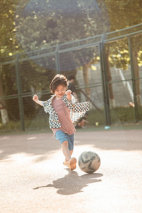 儿童足球摄影照片_夏日儿童人像白天长发小男生操场奔跑踢球摄影图配图