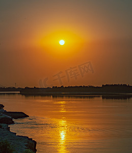 太阳黄色光线摄影照片_夏天自然风光傍晚日落光照户外水面太阳缓缓落下摄影图配图