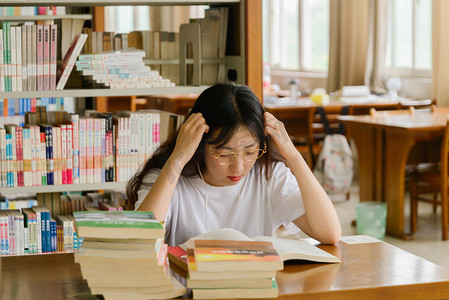 校园人物摄影照片_人像白天大学生图书馆思考摄影图配图