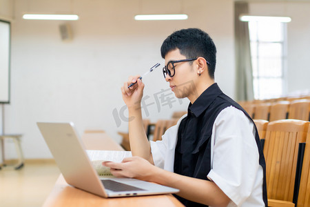 时代青年摄影照片_教室里使用笔记本电脑思考的男大学生