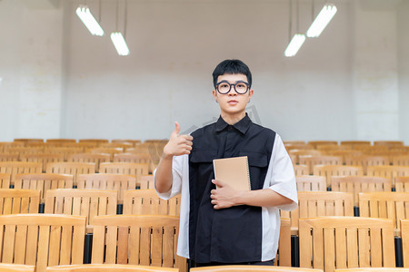 学生点赞摄影照片_课室里使用笔记本学习的男大学生点赞动作