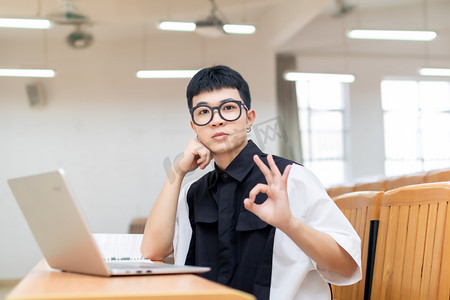 OK摄影照片_教室里使用笔记本电脑OK手势的男大学生