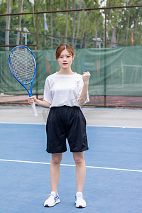 运动女性在网球场手拿网球拍加油打气