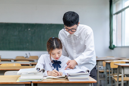 新轴心时代摄影照片_在校园课室里互相辅导的青春男女大学生