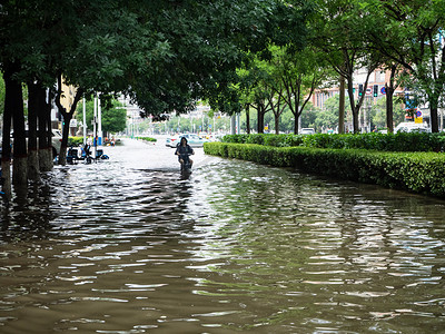 台风卡通摄影照片_被淹的城市白天骑电动暴雨积水中前行摄影图配图