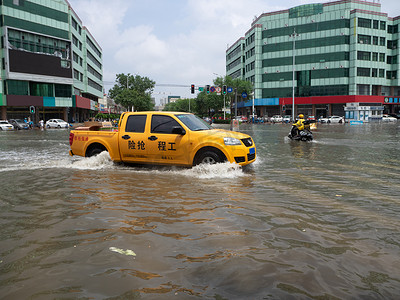 大雨水摄影照片_被淹的城市白天施工抢险车在积水中行驶摄影图配图