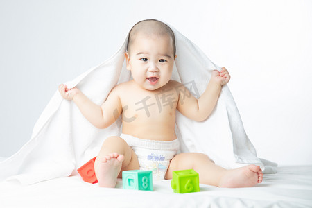 送财猪宝宝摄影照片_婴儿白天披着被子玩耍的男婴室内床上玩玩具笑摄影图配图