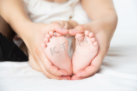 可爱婴儿人物摄影照片_婴儿白天妈妈捧着孩子小脚丫的特写室内摆拍摄影图配图