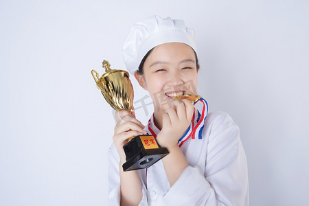 厨师女厨师摄影照片_年轻女厨师白天一个女厨师白背景拿着奖杯咬奖牌摄影图配图