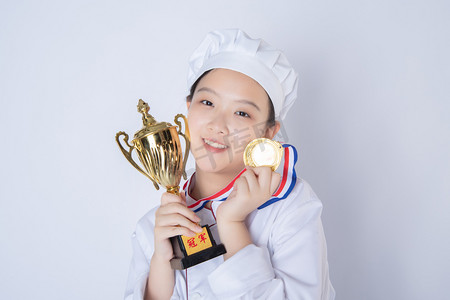 年轻女厨师白天一个女厨师白背景拿着奖杯奖牌靠在脸上摄影图配图