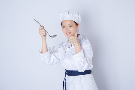 年轻女厨师白天一个女厨师白背景上拿勺点赞手势摄影图配图
