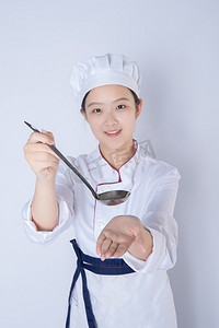 厨师女厨师摄影照片_年轻女厨师白天一个女厨师白背景拿勺成汤送向镜头摄影图配图