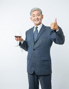 老年人摄影照片_老年生活白天正装老人室内端着酒杯竖大拇指摄影图配图