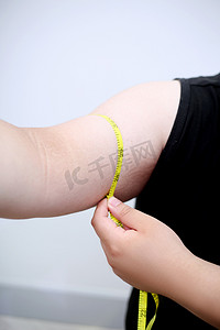 健康管理摄影照片_用尺子测量手臂的肥胖青少年胳膊特写摄影图配图
