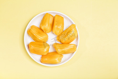 黄色背景上用白色盘子摆放的熟透的菠萝蜜摄影图配图