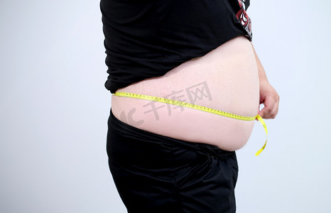 测量头围摄影照片_侧身测量肚子的肥胖青少年特写摄影图配图
