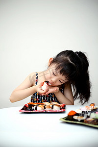 美食摄影照片_室内正在大口吃寿司的小女童人像摄影图配图