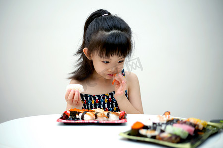可爱寿司摄影照片_室内正在吃寿司的可爱小女孩人像摄影图配图