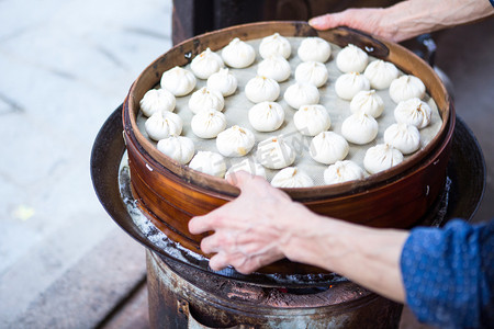 包子店摄影照片_早餐包子蒸煮上午一个人早餐店端举摄影图配图