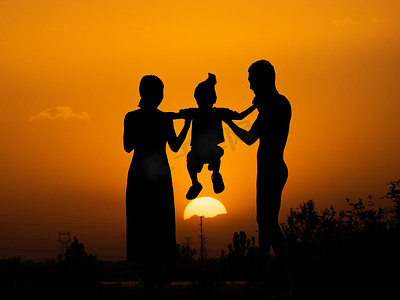 孩子摄影照片_人像剪影夕阳一家三口夕阳下父母抬起孩子摄影图配图