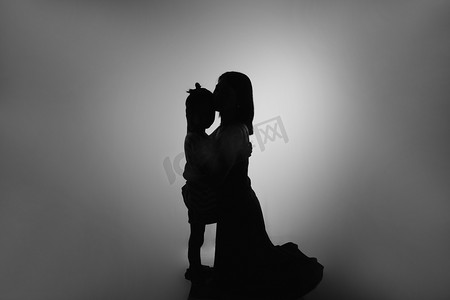 简单黑白摄影照片_人像剪影夜晚母女二人在室内妈妈亲额头摄影图配图