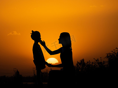 人像剪影夕阳母女二人在夕阳下妈妈手摸女儿脸摄影图配图