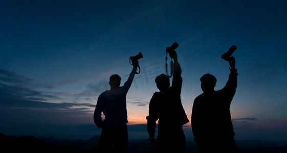 个人摄影照片_剪影夕阳三个人高坡举相机摄影图配图