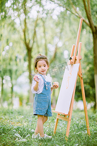 可爱小女孩摄影照片_艺术启蒙画画白天夏天可爱小女孩户外草地画画写生摄影图配图