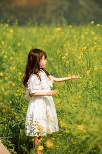 开心的女孩子摄影照片_可爱的小女孩油在菜花田手摸油菜花摄影图配图